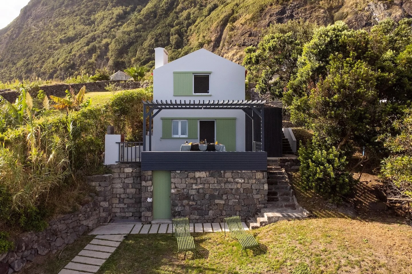 Renovated white cottage with green shutters set into volcanic hillside, Azores