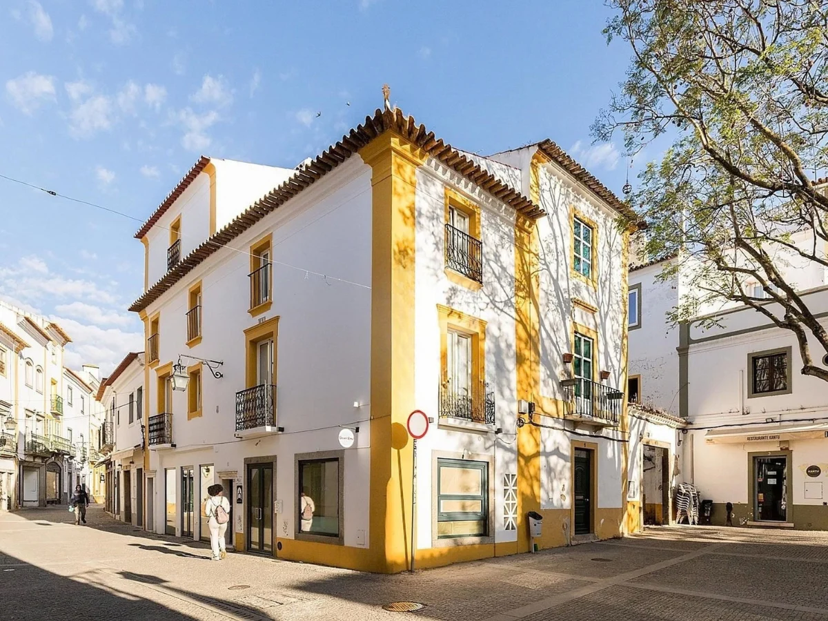 A white townhouse with yellow trim on a sunny square in the old town of Evora